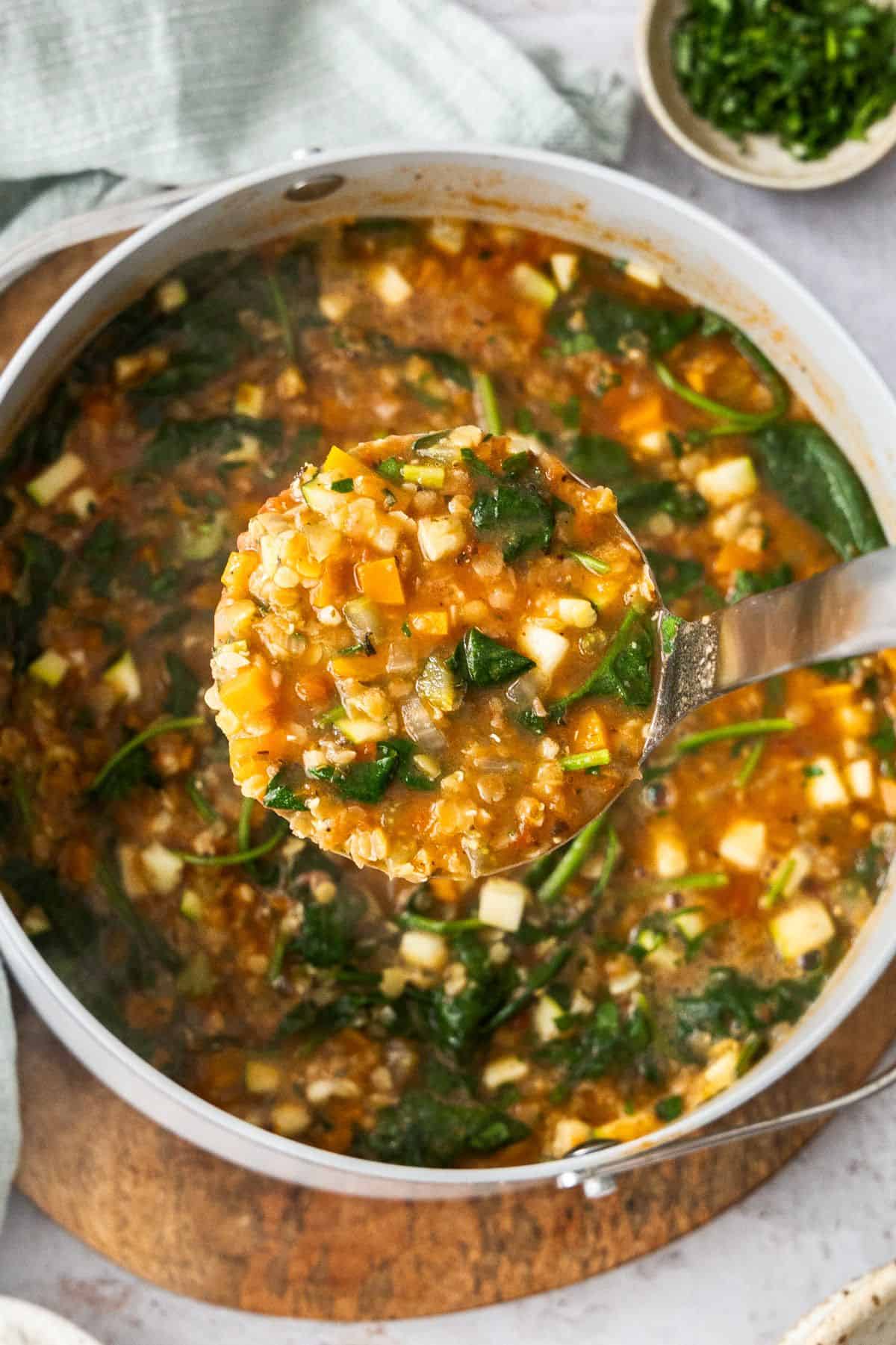 Large saucepan with the cooked Red Lentil Soup, with a soup ladle lifting up a serve of the soup.