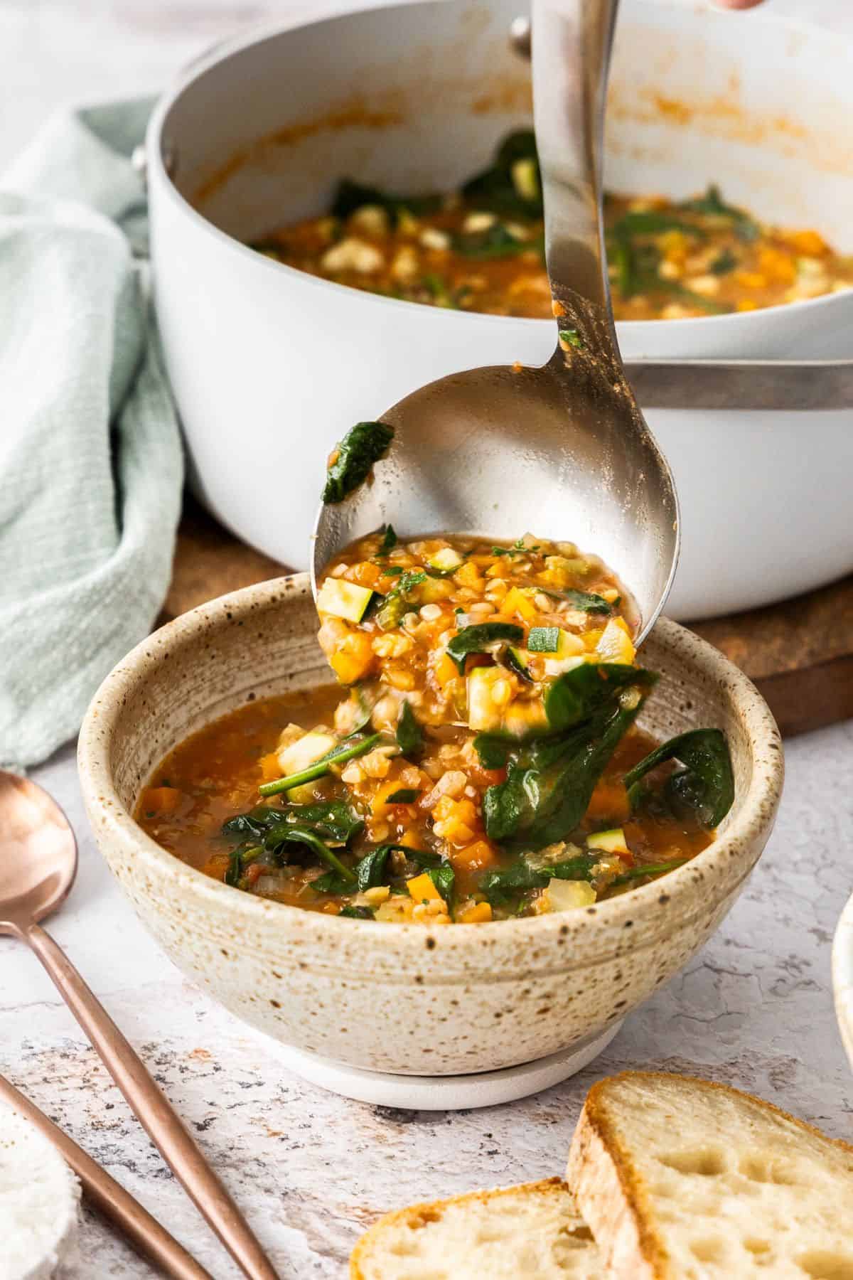 Ladling a serve of Red Lentil Soup into a round beige bowl.