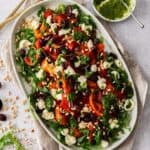 Oval platter with Roasted Capsicum (Red Pepper) Salad, with some serving utensils on the side.