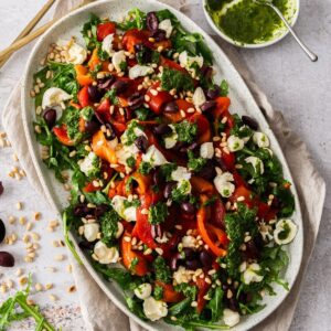 Oval platter with Roasted Capsicum (Red Pepper) Salad, with some serving utensils on the side.