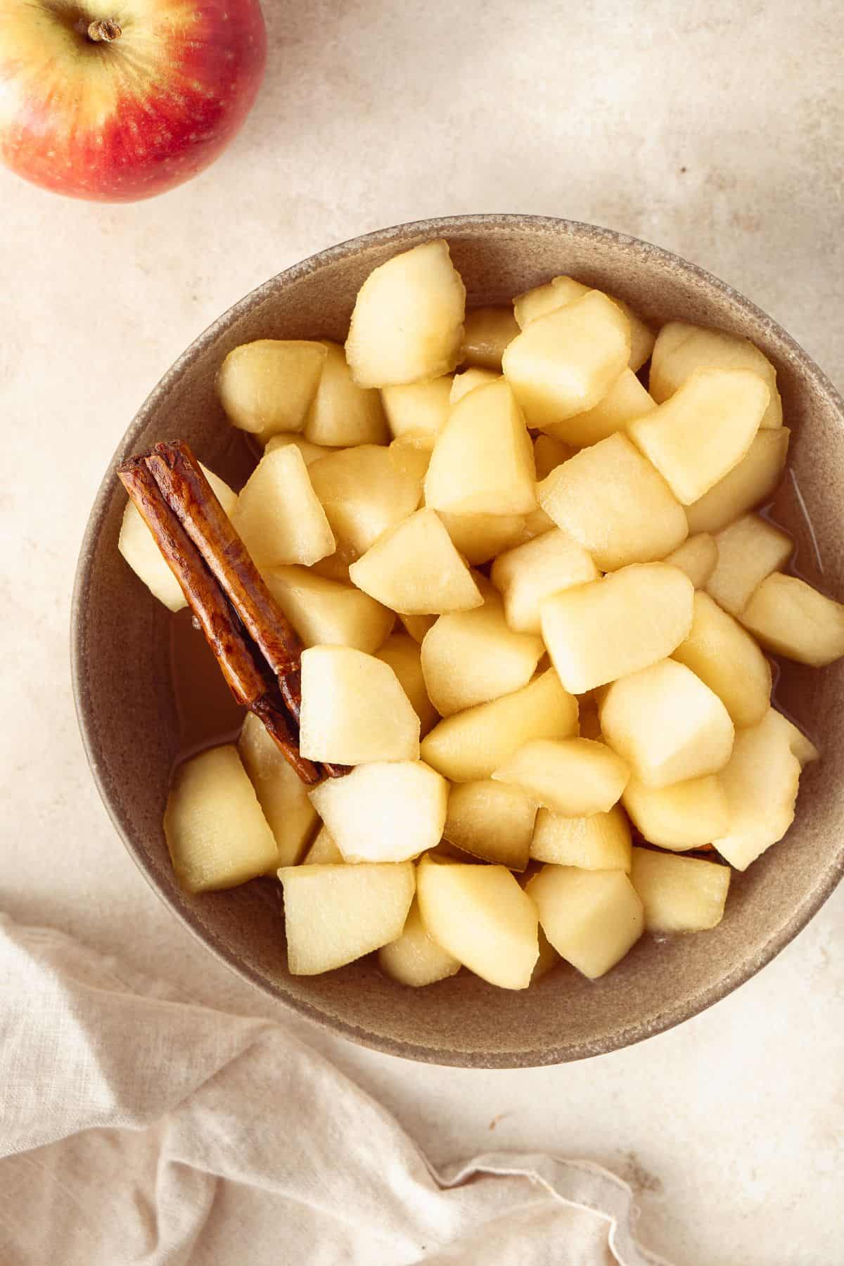 Small round dish of Stewed Apples, with a cinnamon stick sitting in the bowl.