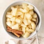 Round bowl of Stewed Pears, with two cinnamon sticks and a spoon sitting in bowl.