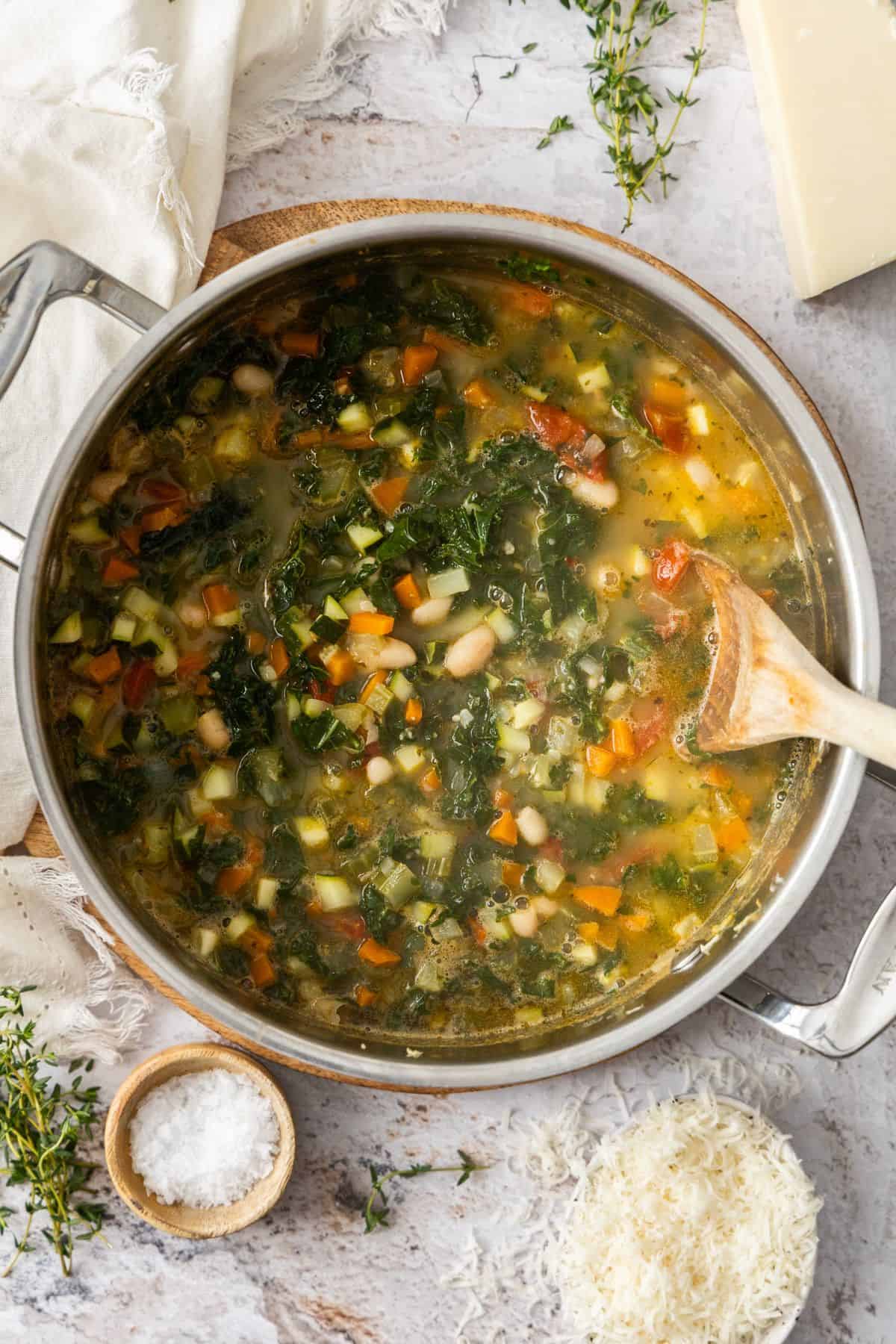 Large saucepan with the cooked Mediterranean Cannellini Bean Soup, with a wooden spoon resting in the pot.