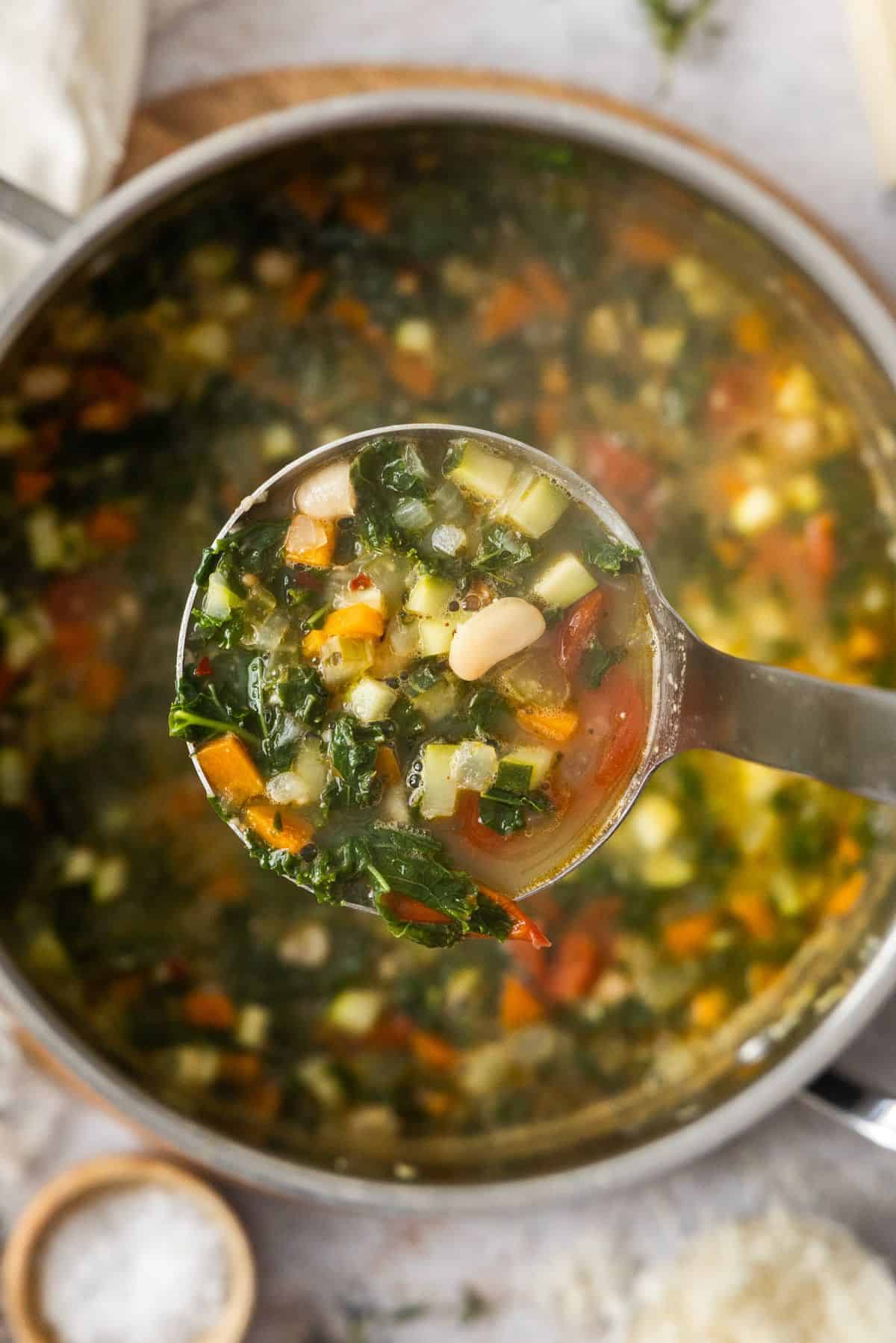 Large saucepan with the cooked Mediterranean Cannellini Bean Soup, with a soup ladle lifting up a serve of the soup.