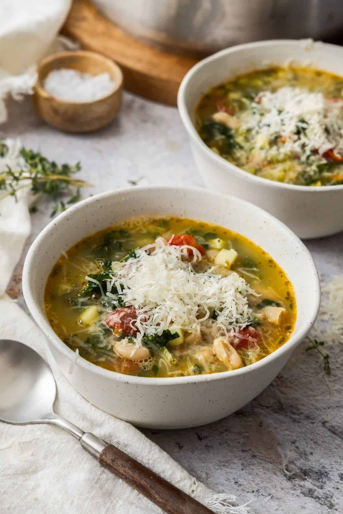 Two bowls of Mediterranean Cannellini Bean Soup, topped with some grated Parmesan cheese.