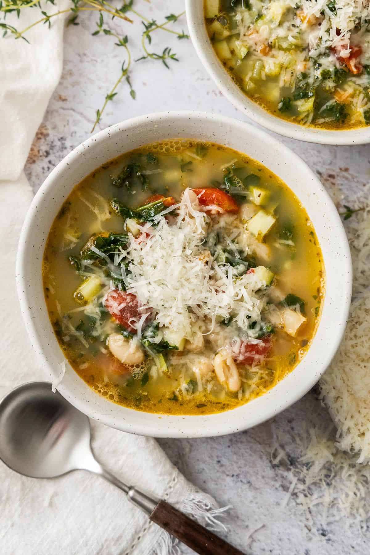 Two bowls of Mediterranean Cannellini Bean Soup, topped with some grated Parmesan cheese.