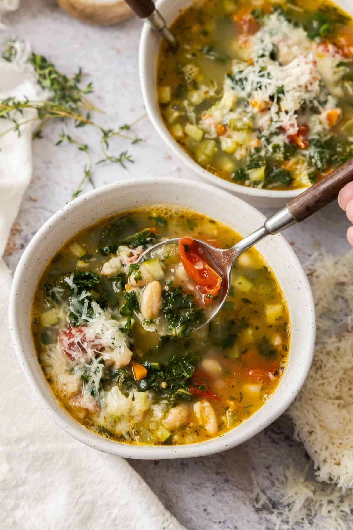 Two bowls of Mediterranean Cannellini Bean Soup, one with a spoon dipping in to lift some soup out.