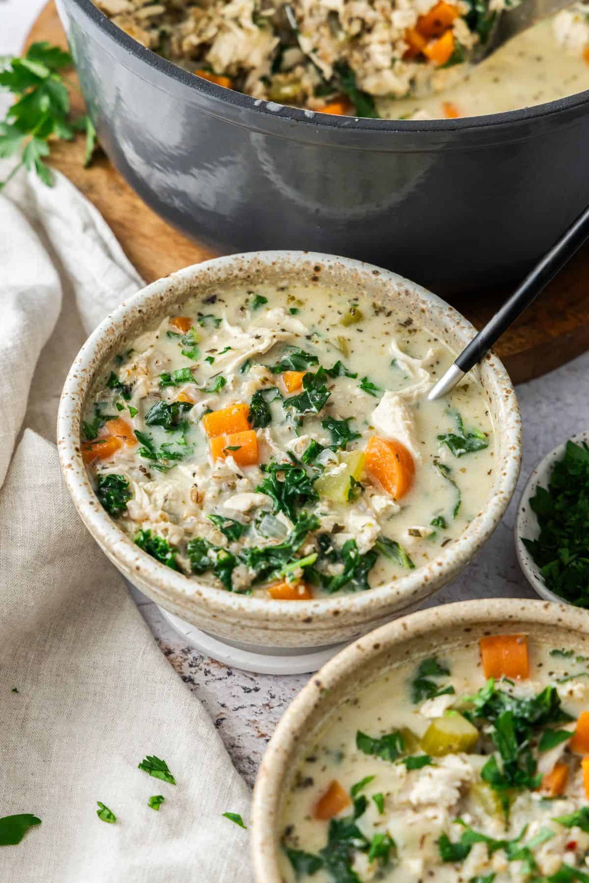 Two bowls with serves of Creamy Chicken and Barley Soup, one with a spoon in it.