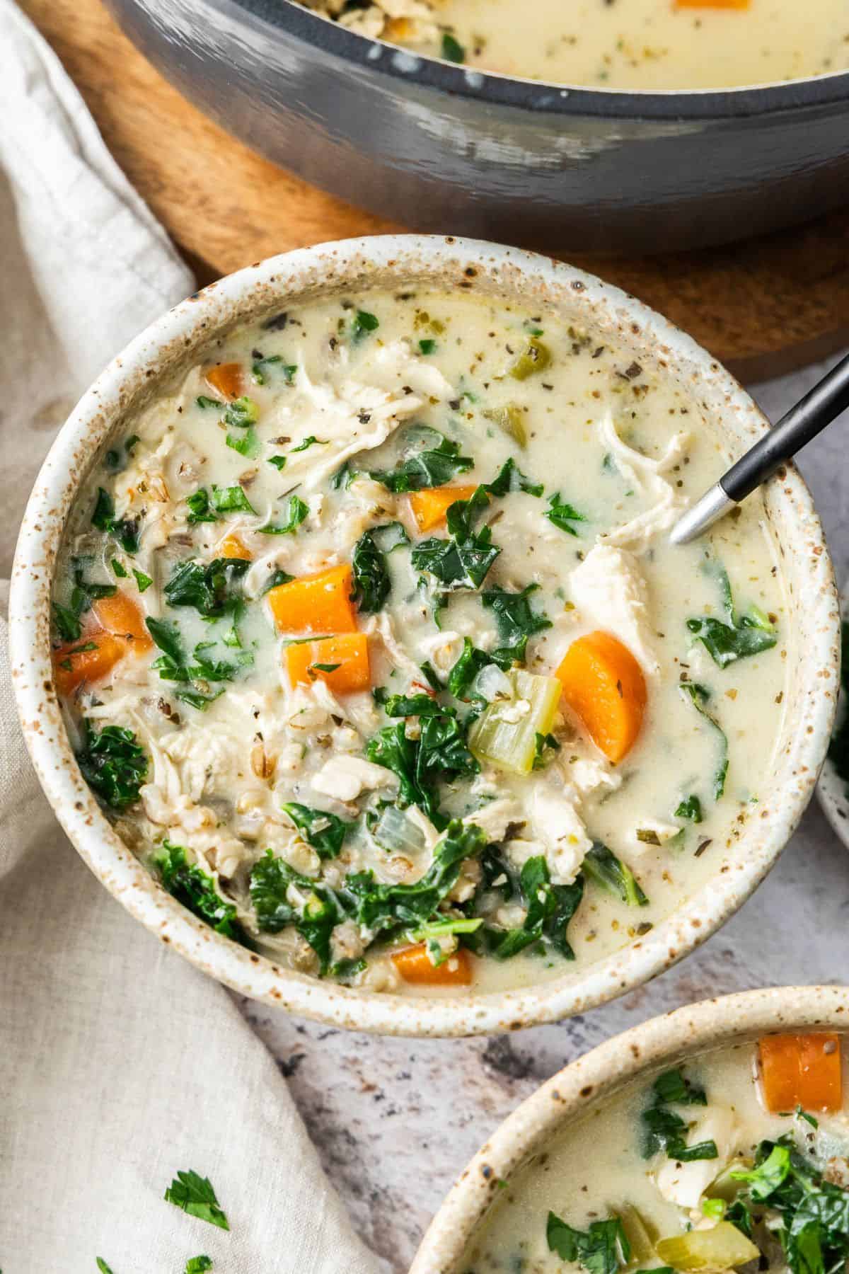 Round bowl with a serving of Creamy Chicken and Barley Soup, with a spoon sitting in the bowl.