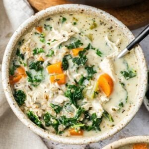 Round bowl with a serving of Creamy Chicken and Barley Soup, with a spoon sitting in the bowl.