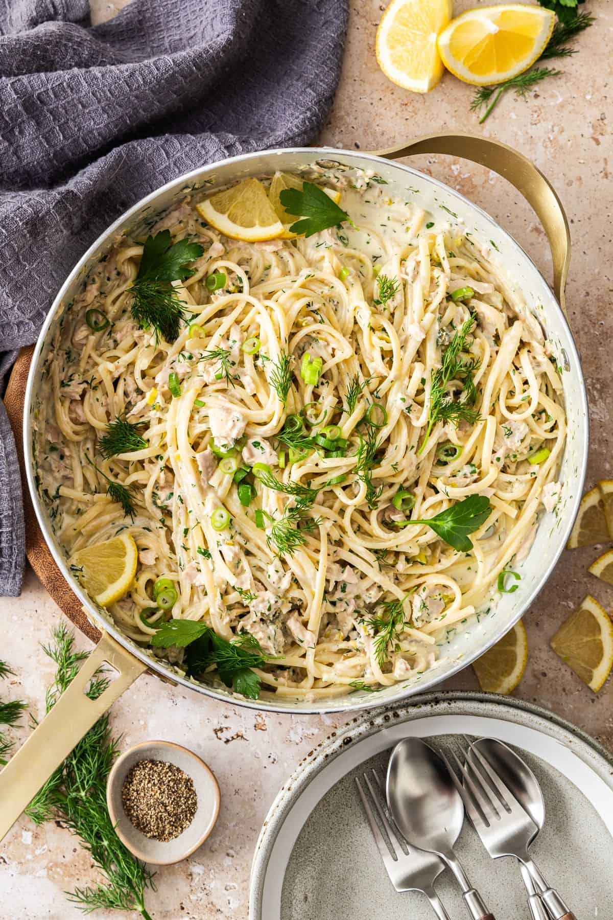 Large frying pan filled with Creamy Tuna Pasta, topped with fresh dill, parsley and some slices of lemon.