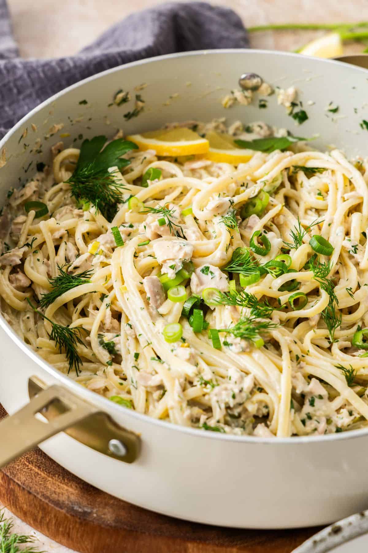 Large frying pan filled with Creamy Tuna Pasta, topped with fresh dill, parsley and some slices of lemon.