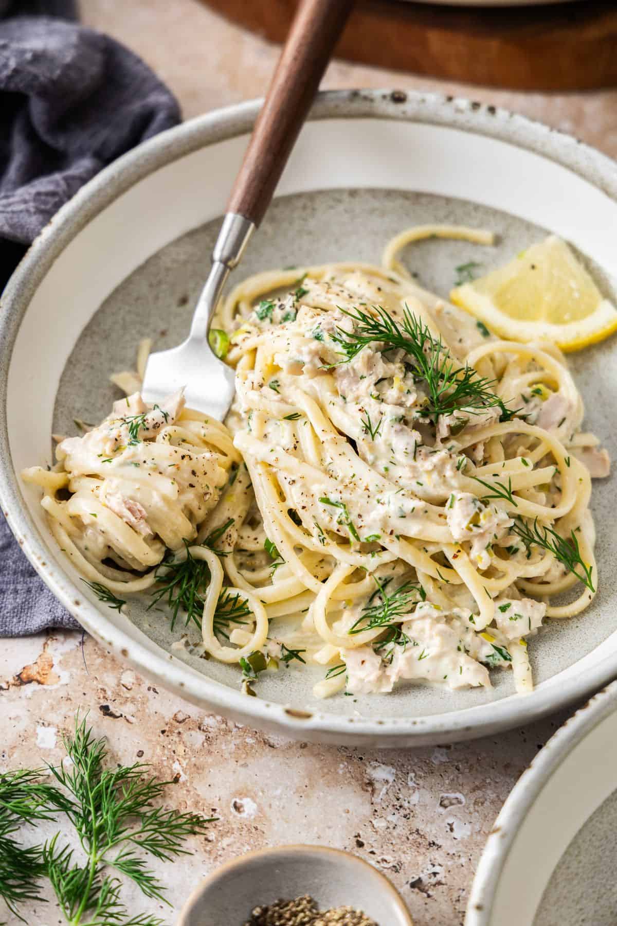 A round grey and white bowl with a serve of Creamy Tuna Pasta, with a fork scooping up a bite.