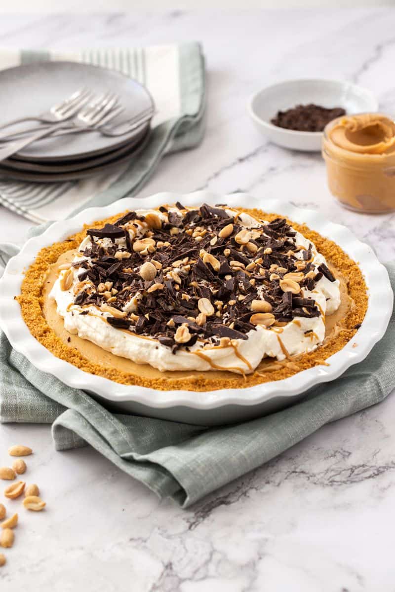 Peanut Butter Pie garnished with whipped cream, chocolate shavings and peanuts, sitting on a grey towel.