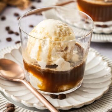 A glass with Affogato - coffee, liqueur and ice cream - sitting on a white fluted saucer, with a bronze spoon.