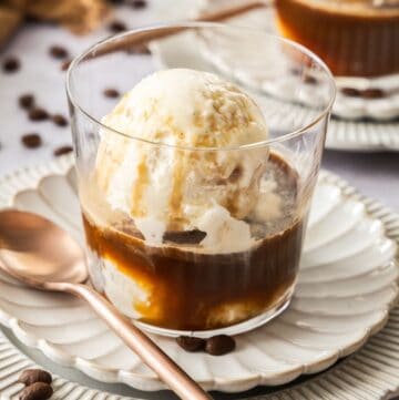 A glass with Affogato - coffee, liqueur and ice cream - sitting on a white fluted saucer, with a bronze spoon.