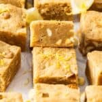 Cut squares of Lemon Blondies sitting on baking paper, with one on an angle to show the texture.