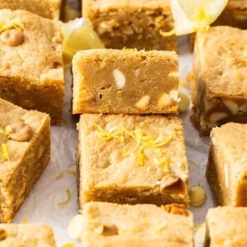 Cut squares of Lemon Blondies sitting on baking paper, with one on an angle to show the texture.