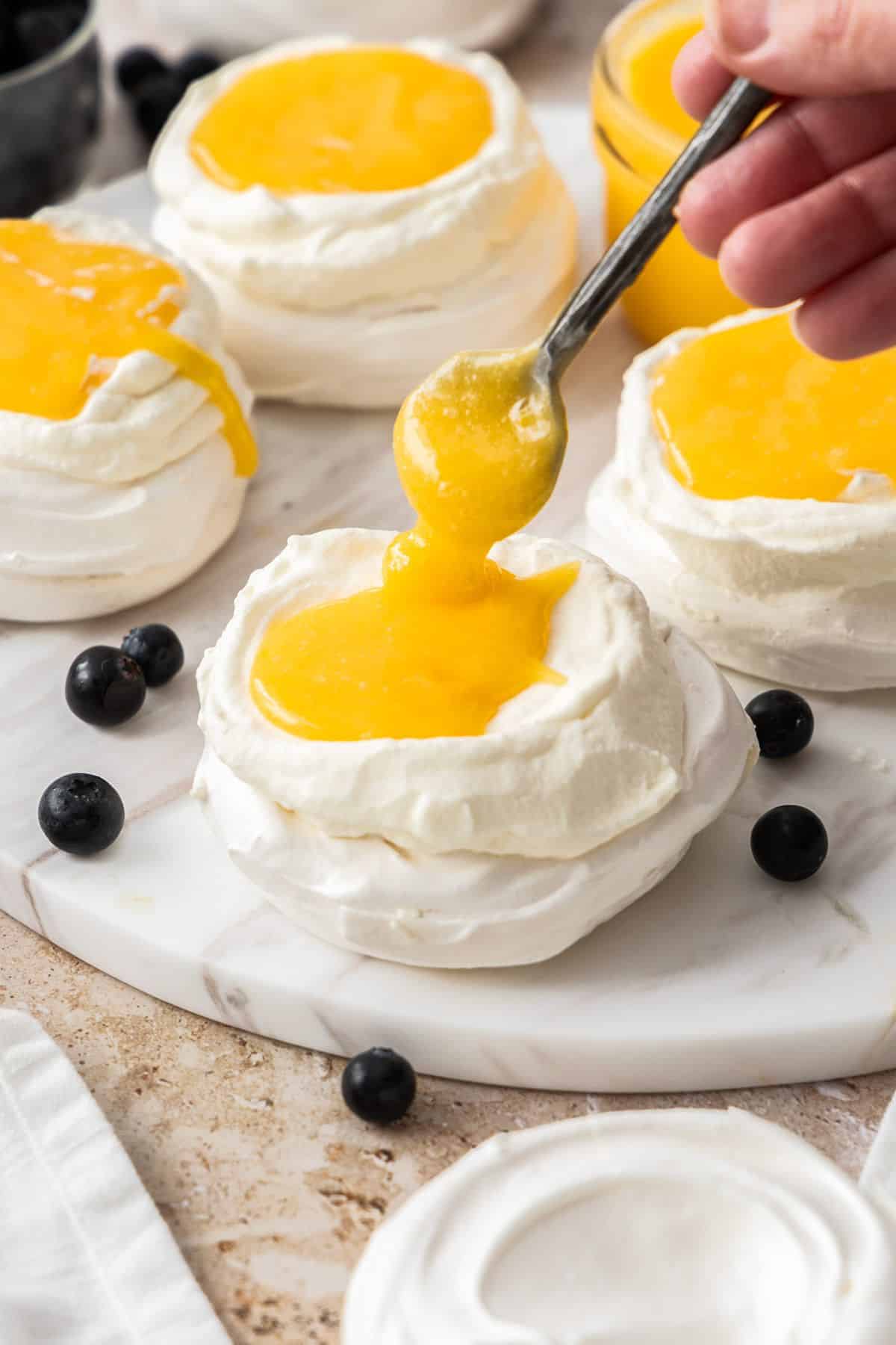 A spoon topping the meringue nests with some lemon curd.