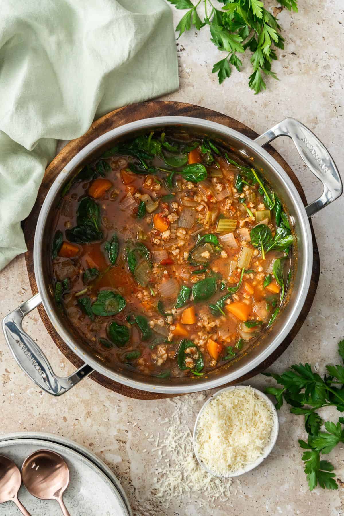 Pot of Mediterranean Vegetable and Barley Soup sitting on a round wooden board.