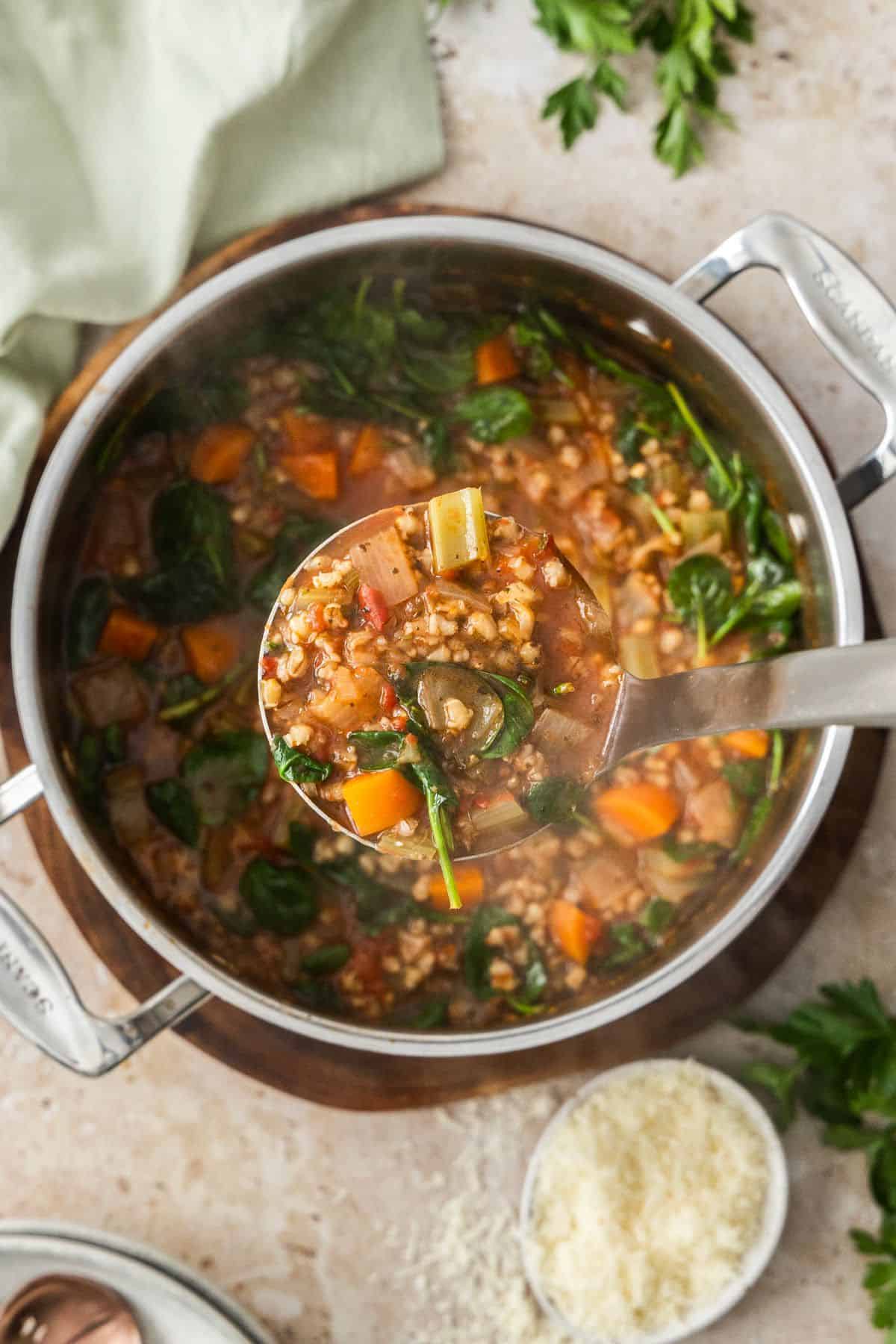 A soup ladle holding up some Mediterranean Vegetable and Barley Soup, ready to put into a bowl.