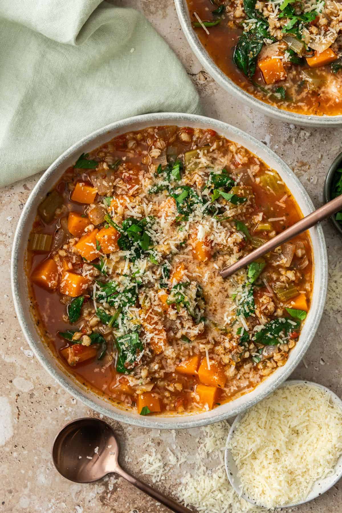 Two bowls with serves of Creamy Chicken and Barley Soup, one with a spoon in it.