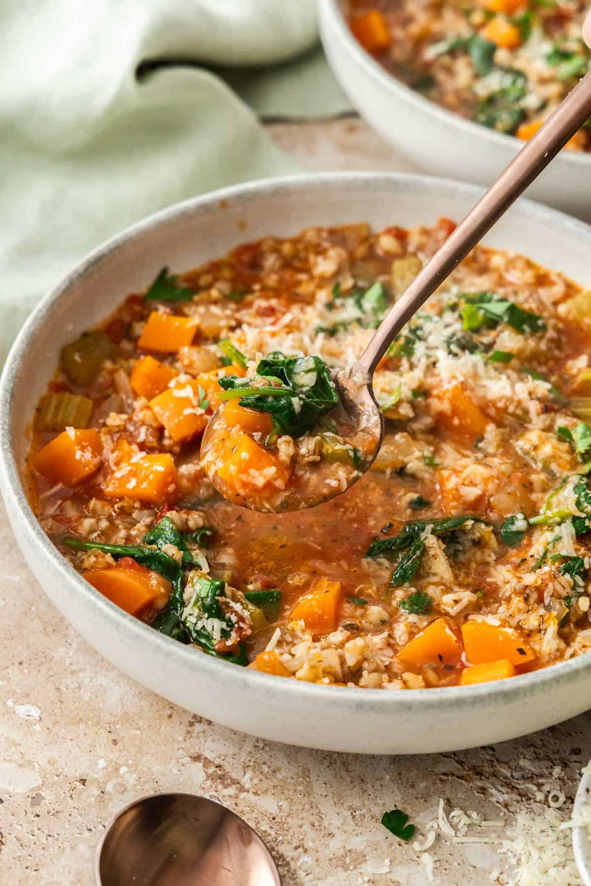 Bowl of Vegetable and Barley Soup, with a spoon lifting up a mouthful of soup.