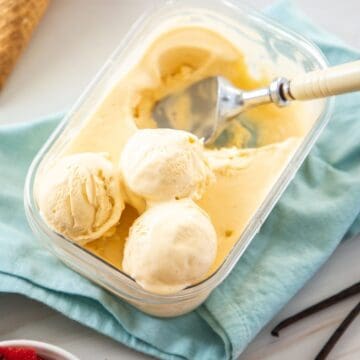 Plastic container of ice cream, with some serves scooped out, with some ice cream cones and a bowl of strawberries on the edge.