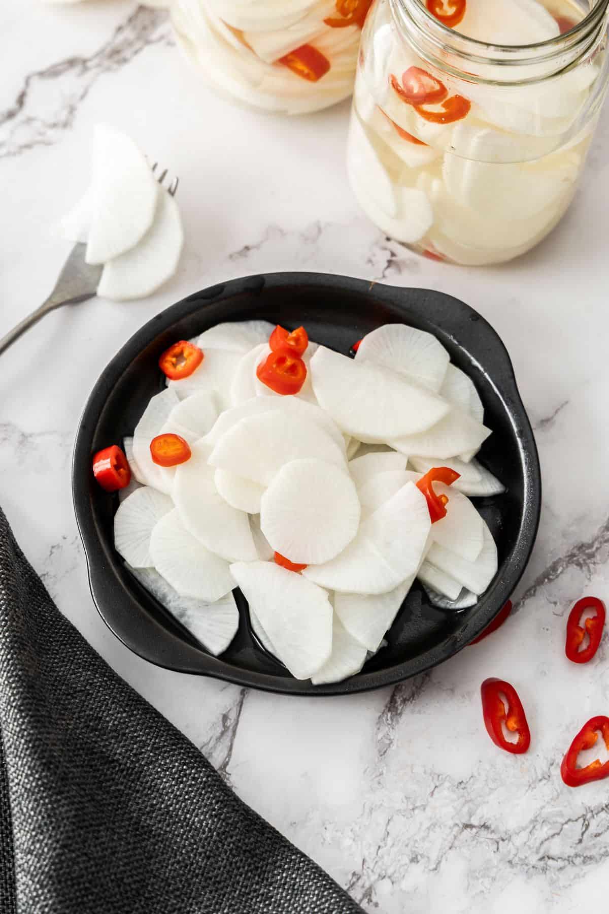 Round black plate, with Pickled Daikon and some of the chilli pieces.