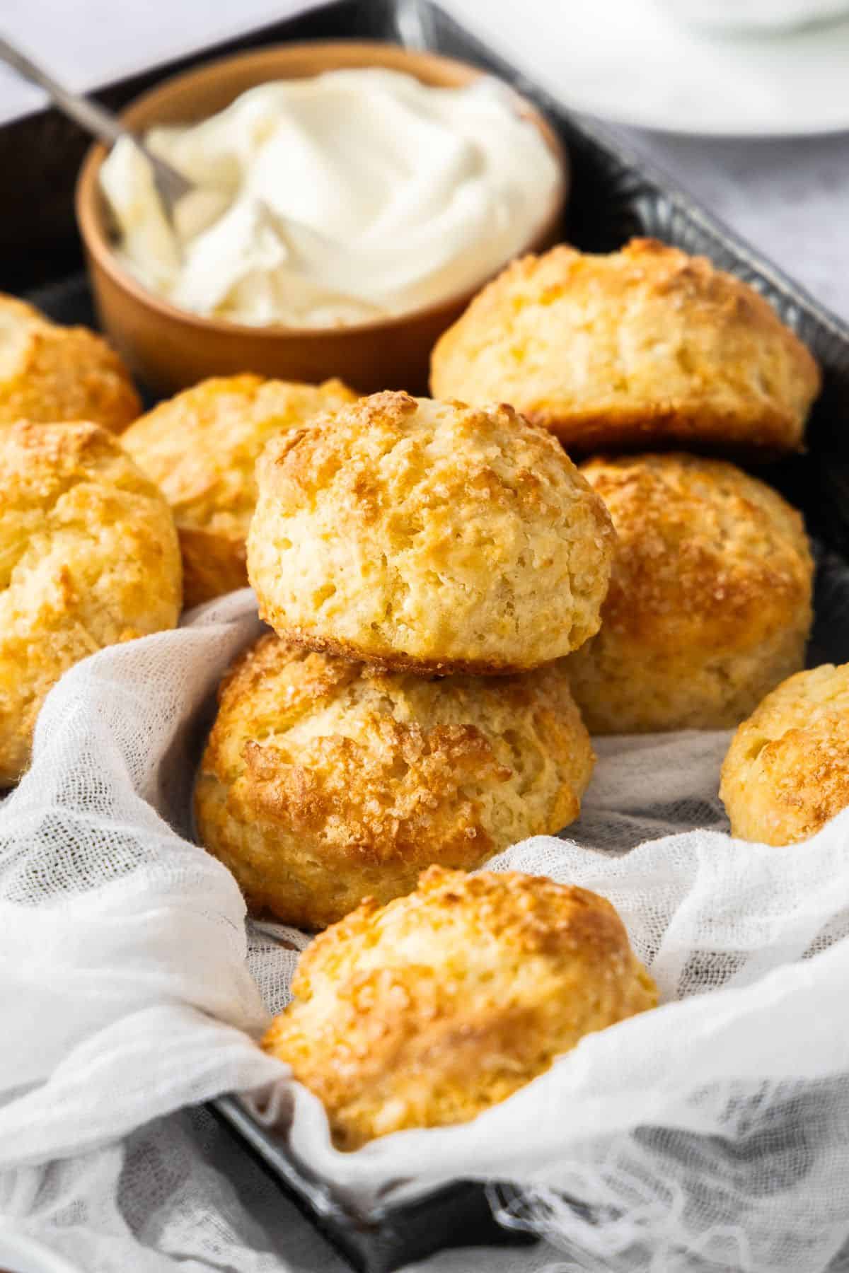 Black tray with a white cloth, full of Buttermilk Scones, with a small dish of cream in the corner of the trays.