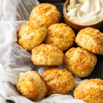 Black tray with a white cloth, full of Buttermilk Scones, with a small dish of cream in the corner of the trays.