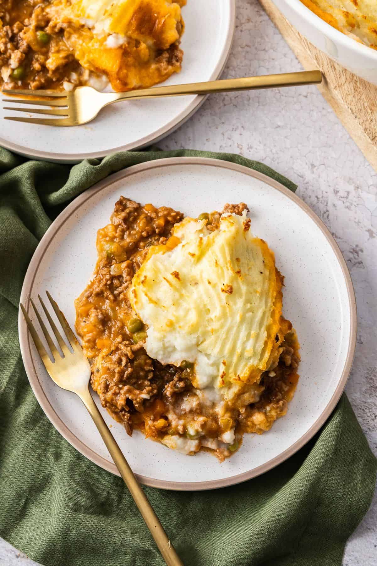 Two white round plates with servings of Cottage Pie on them, with a gold fork on each plate.