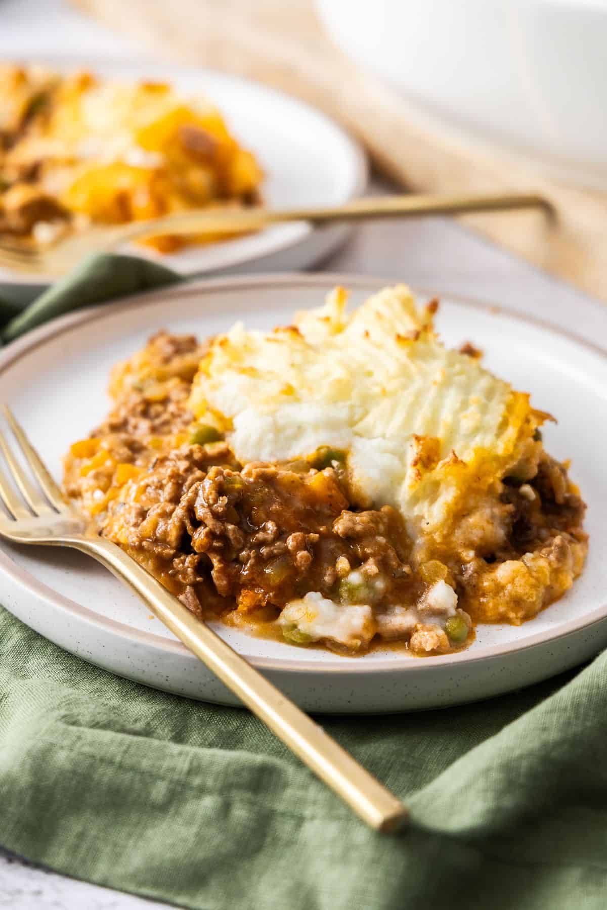 Two white round plates with servings of Cottage Pie on them, with a gold fork on each plate.