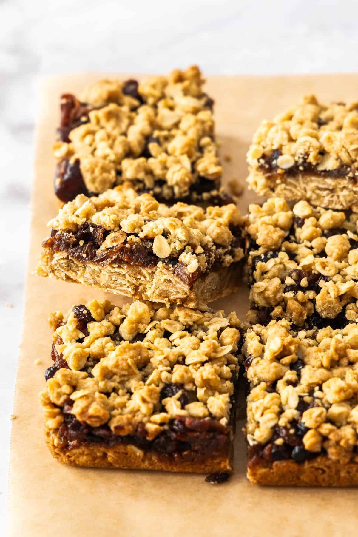 Six cut pieces of Fruit Mince Oatmeal Bars, one of them positioned on an angle to show filling, sitting on some brown paper.