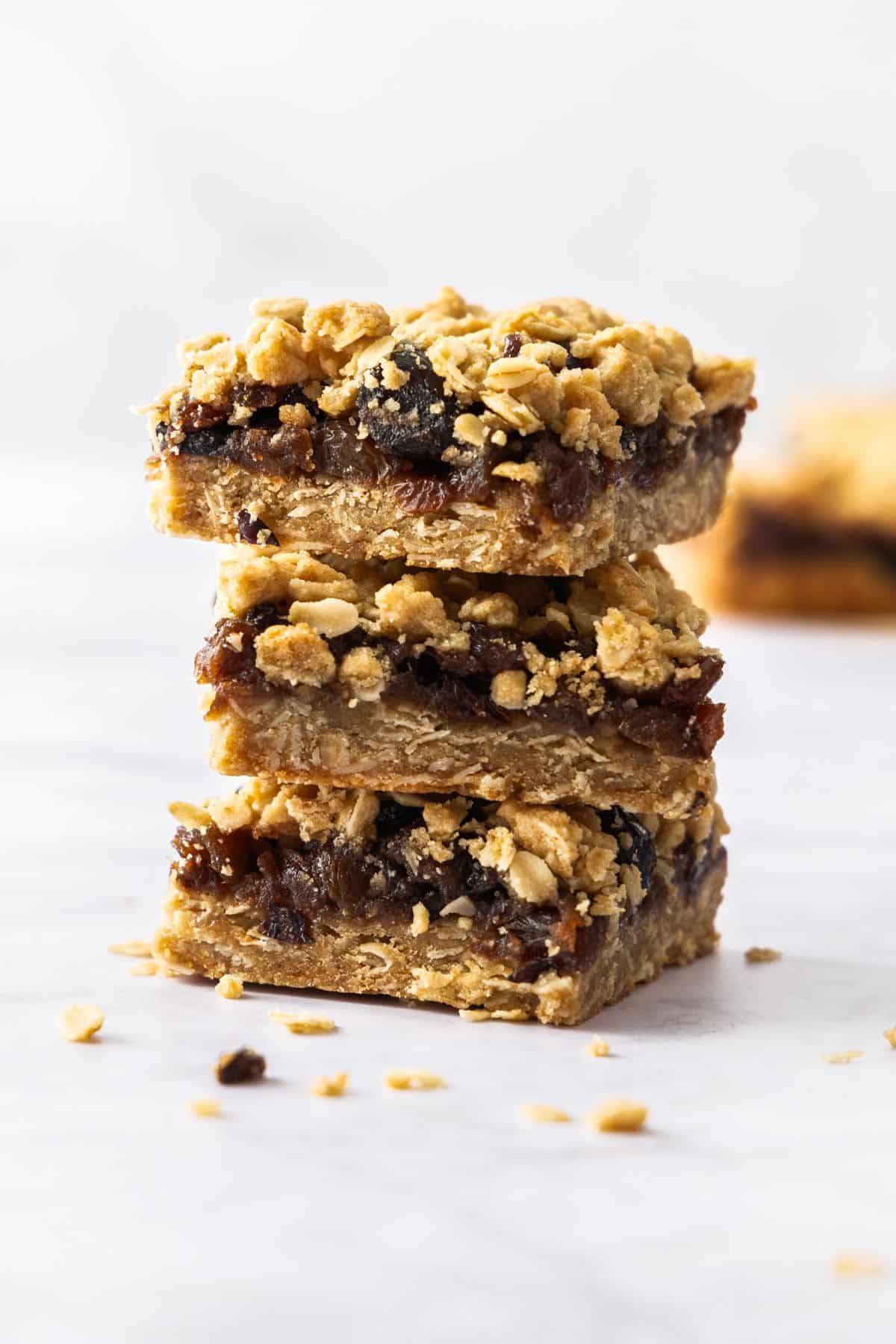 Stack of three pieces of Fruit Mince Oatmeal Bars sitting on a marble benchtop.