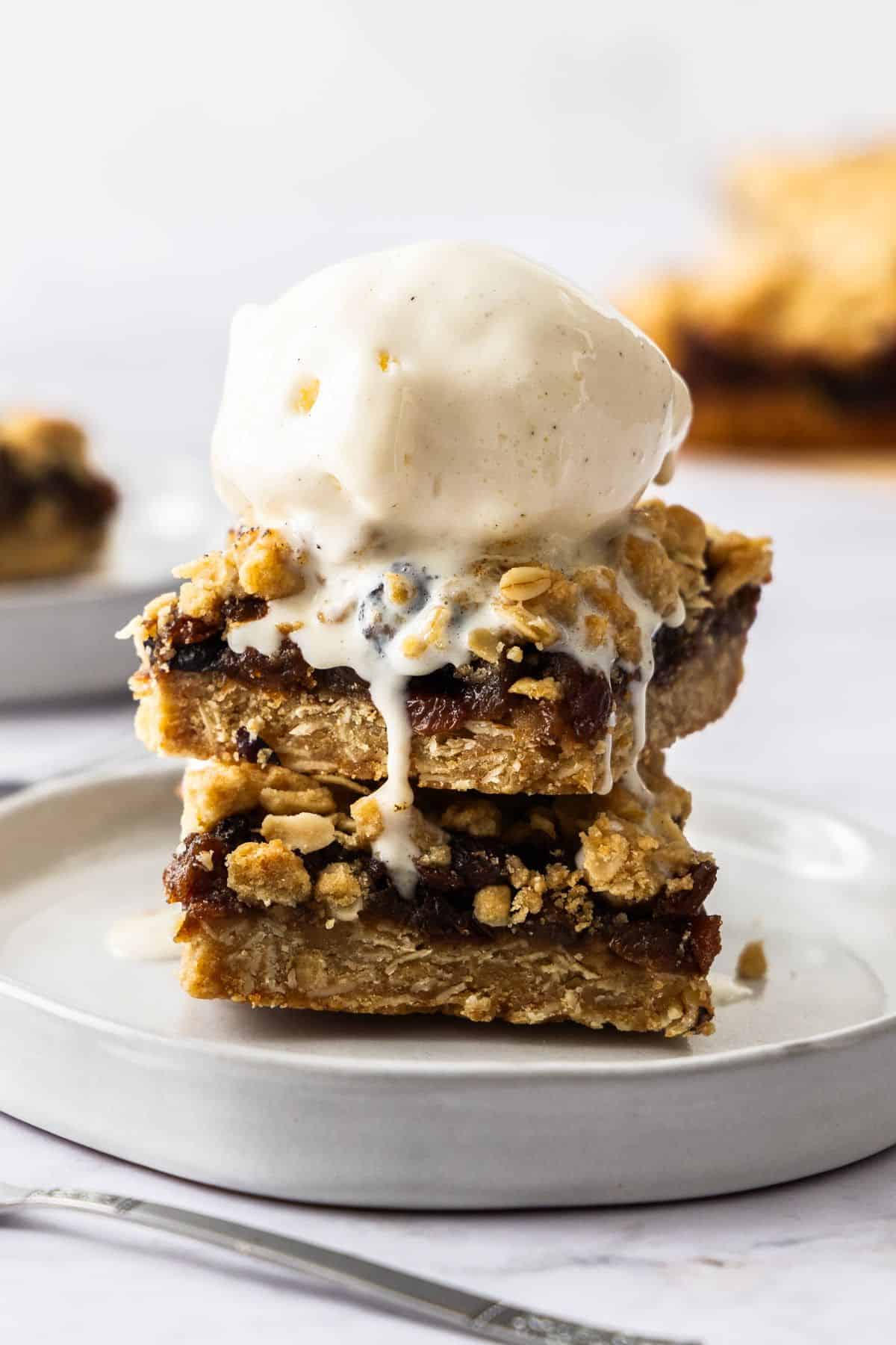 Two pieces of Fruit Mince Oatmeal Bars sitting on a round grey plate, with a scoop of vanilla ice cream on top.