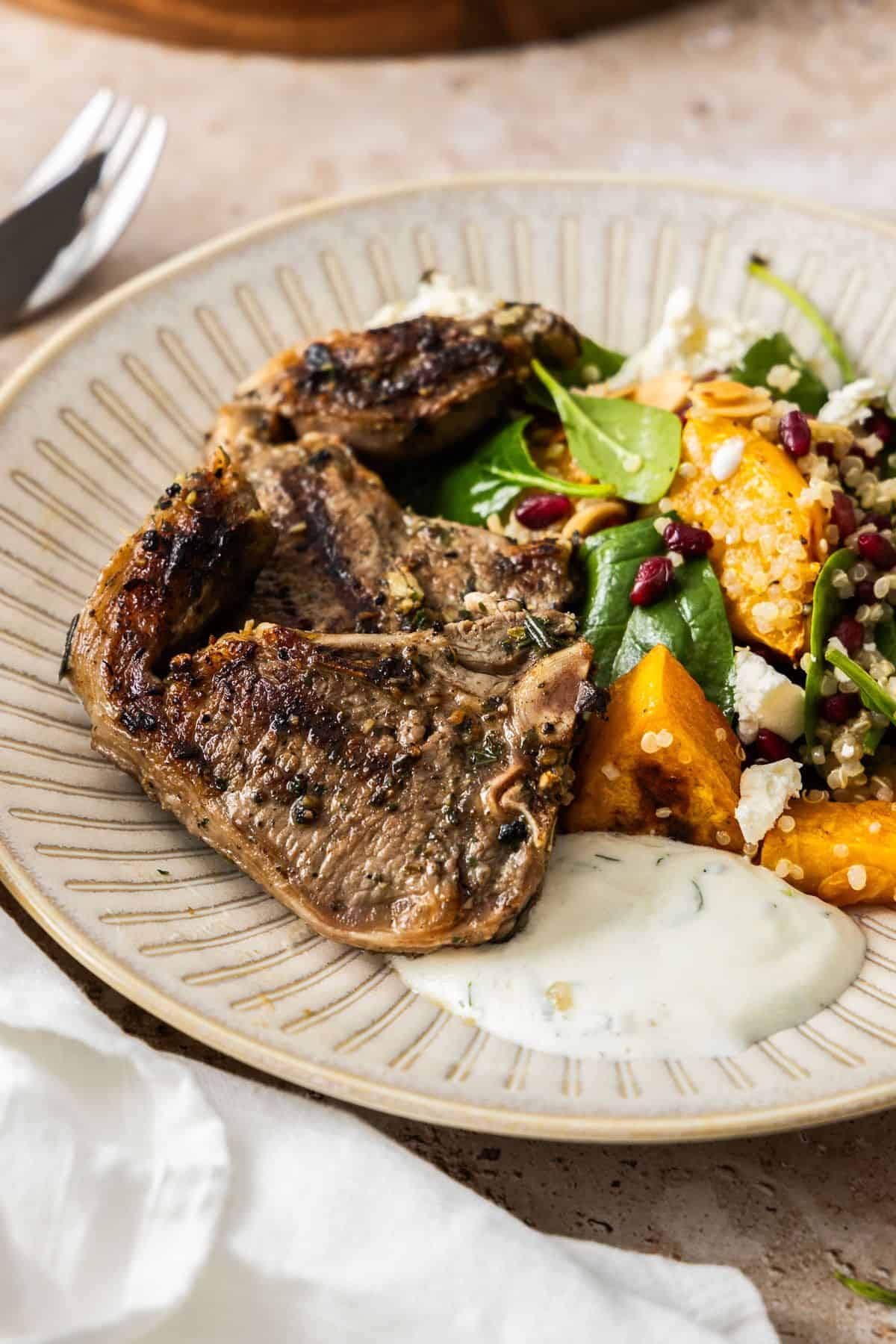 Round brown plate with a serve of lamb loin chops, pumpkin and spinach salad and yoghurt sauce.