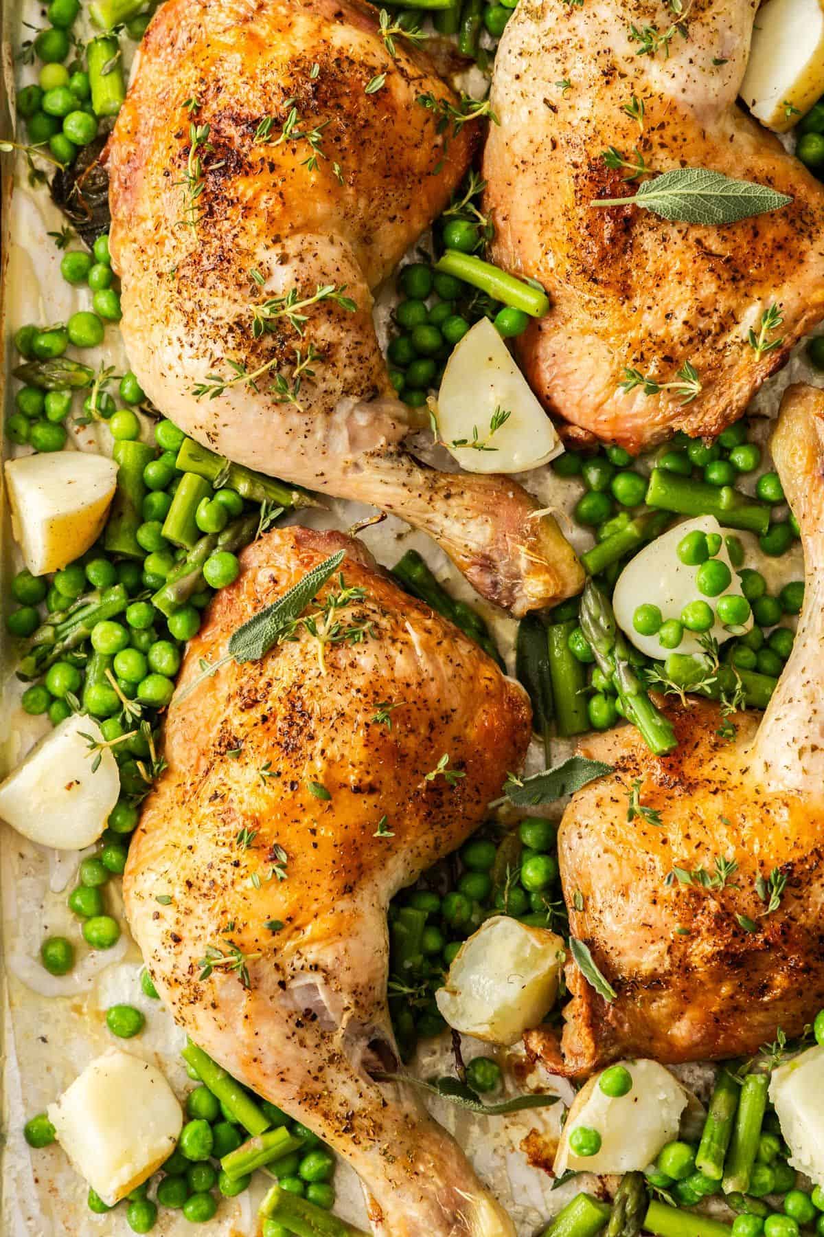 Roasted Chicken Marylands on a baking tray, surrounded by some cubes of potatoes, peas and green beans.