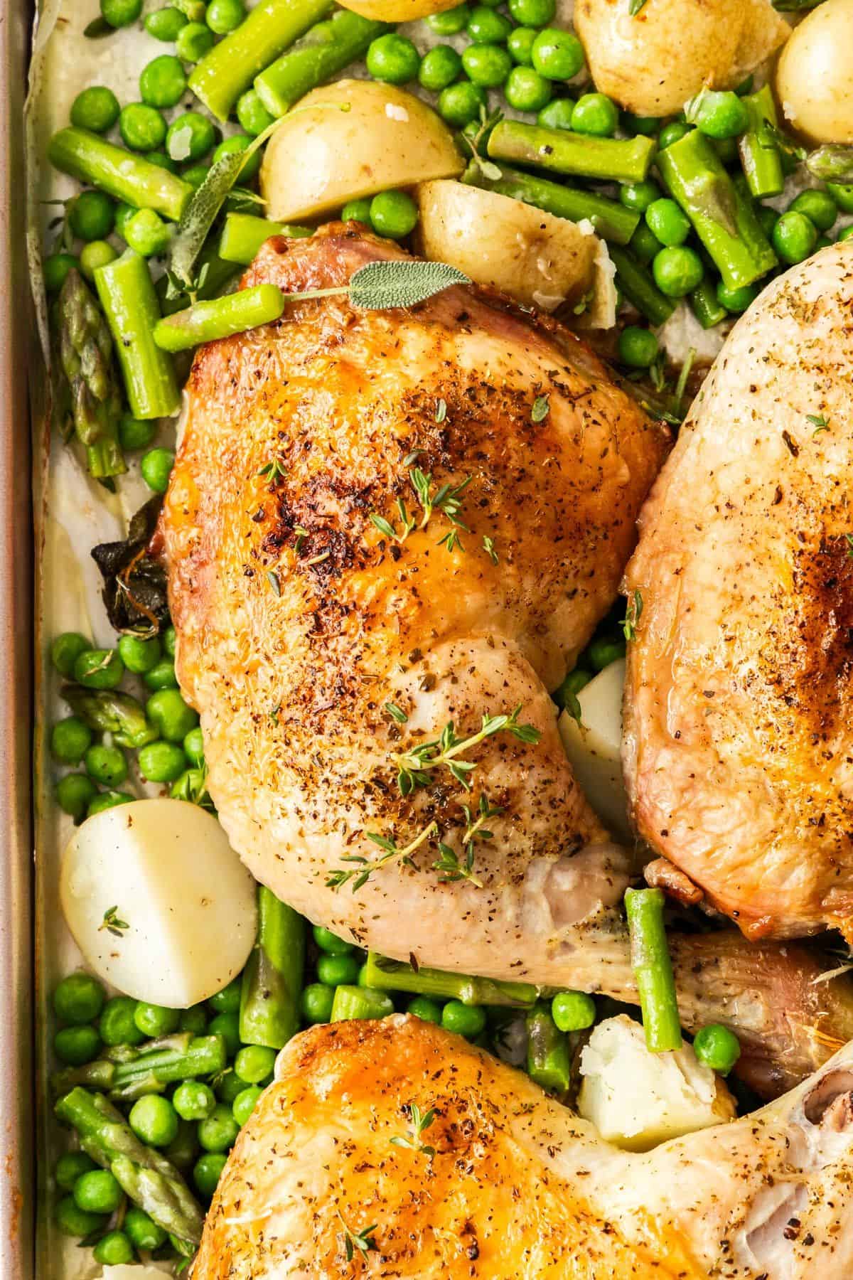 Roasted Chicken Marylands on a baking tray, surrounded by some cubes of potatoes, peas and green beans.