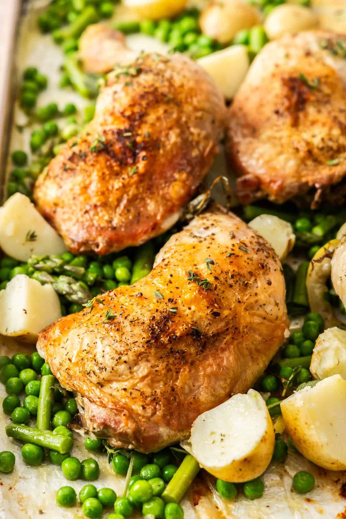 Roasted Chicken Marylands on a baking tray, surrounded by some cubes of potatoes, peas and green beans.