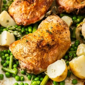 Roasted Chicken Marylands on a baking tray, surrounded by some cubes of potatoes, peas and green beans.