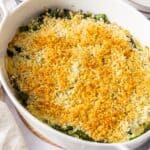 White oval dish of baked Asparagus Gratin, sitting on a white cloth.