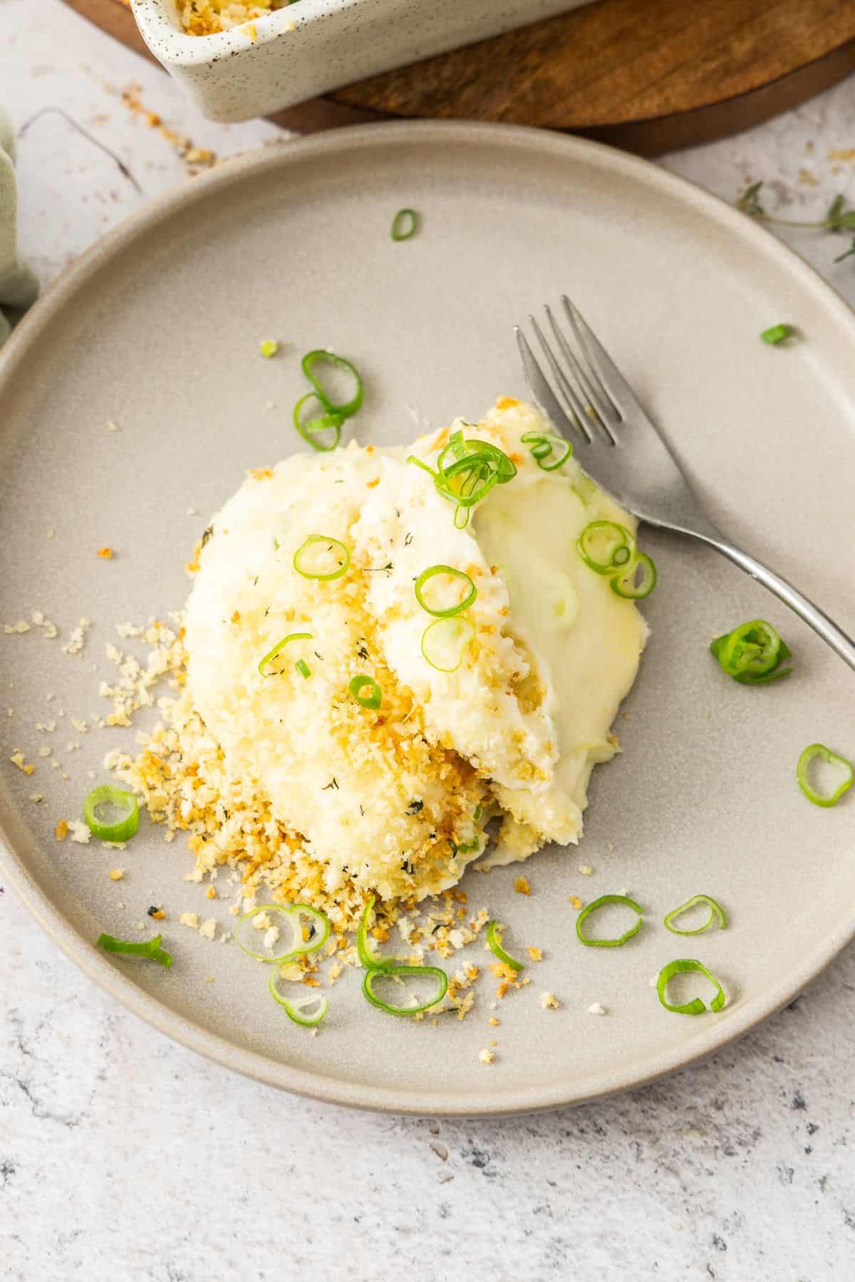 Round grey plate with a serve of Baked Mashed Potatoes, with a fork alongside.