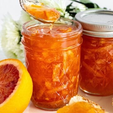 Two jars of Orange Marmalade, one with a spoon lifting a scoop of marmalade out of it.