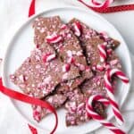 Round white dish of Candy Cane Chocolate Bark, with some red ribbon and additional candy canes on the edge.