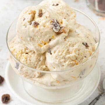 Four scoops of Fruit Mince Ice Cream in a glass bowl, sitting on a small white plate, with a silver spoon on the edge.