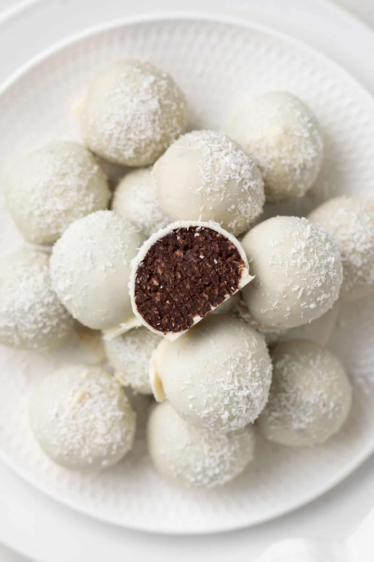 Round white plate with a stack of Coconut Truffles, one cut in half to show the inside.