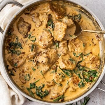 Large silver frying pan, with the cooked Creamy Pork Tenderloin, with a serving spoon in the pot.