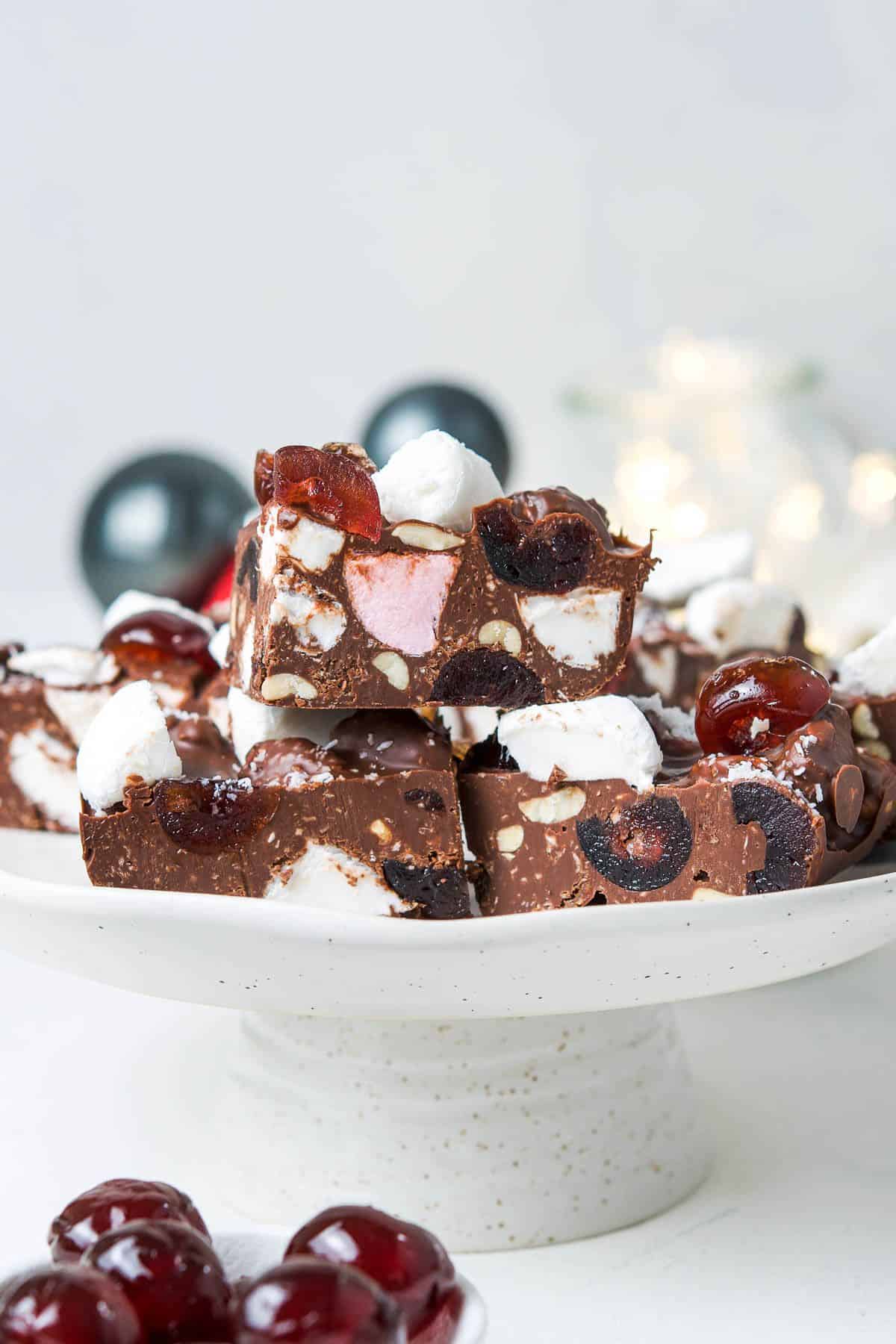 Round tall cake stand with cut pieces of Rocky Road, sitting on a white bench top.