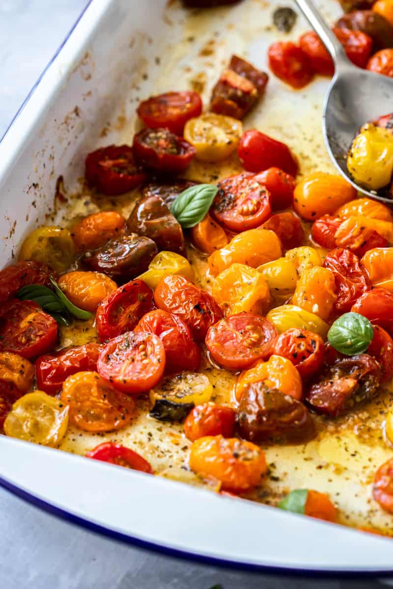 Baking dish with Roasted Cherry Tomatoes, with a silver spoon scooping into them.